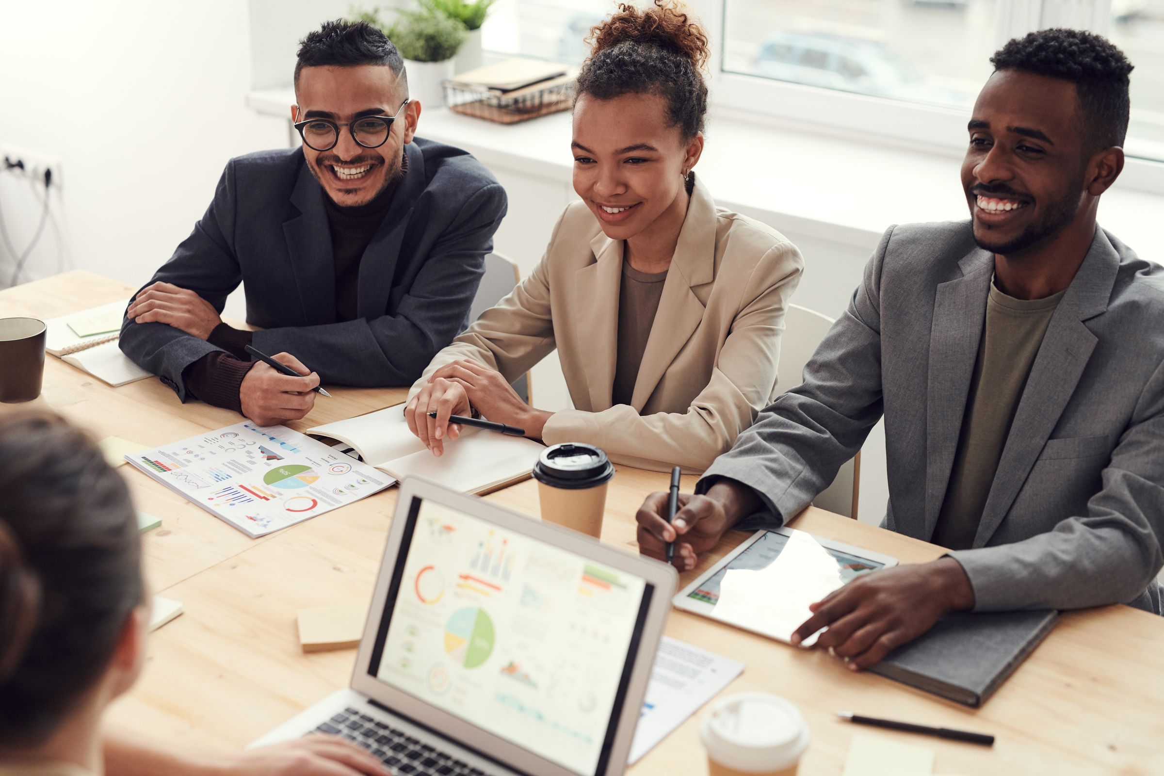 Three smiling professionals reviewing charts together at a bright office table